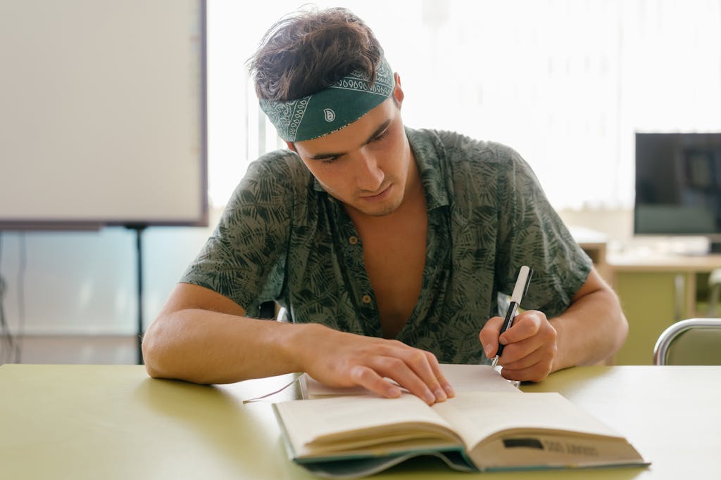 BLOG VIEW Naijastudyhub Young man intensely studying with a notebook at a desk indoors, focusing on research and writing.
